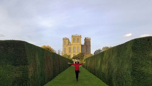 Woman stands with open arms in the formal garden of Hardwick Hall