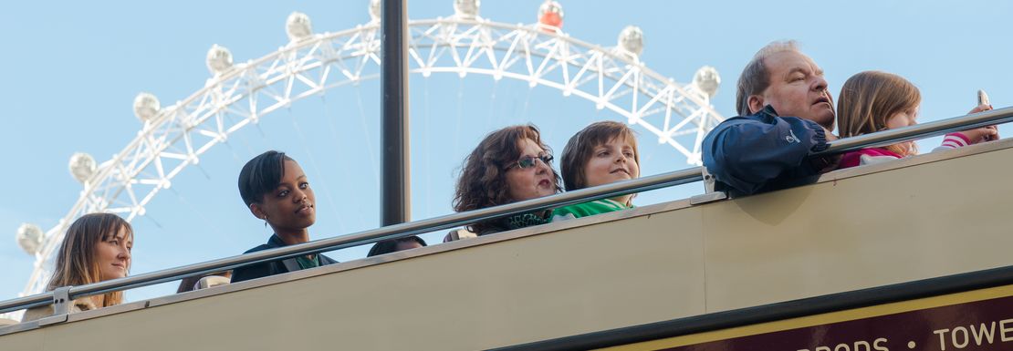 A bus full of visitors to London drive through London with the London Eye in the background