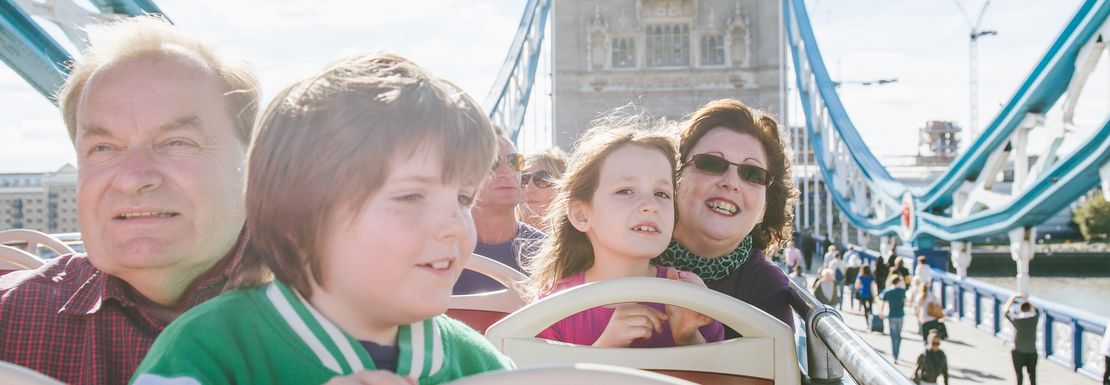 A family smiles in the sunshine as it drives over Tower Bridge