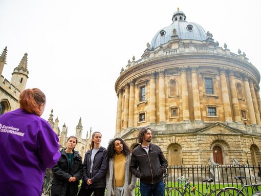 A tour guide leads a group on the Oxford walking tour and stops at an impressive building