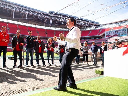 An enthusiastic tour guide takes visitors down to the pitch at Wembley Stadium