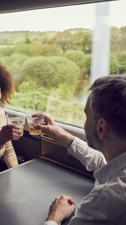 A couple enjoying a drink while travelling by train from Bath, sitting at a table,