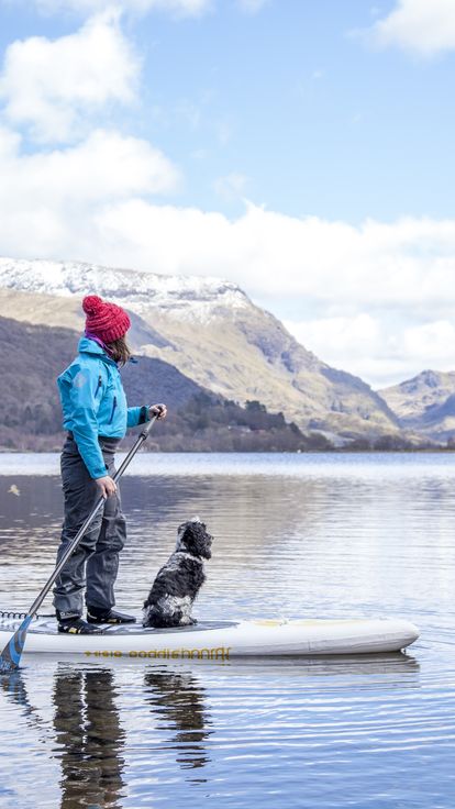 Woman and dog on a paddle-board on lake near mountains