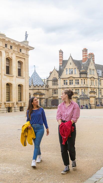 Two women walk across a courtyard among heritage buildings in Oxford