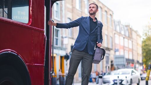 A man stands at the end of a red bus in London