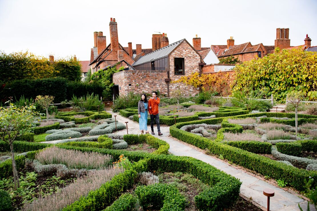 A couple standing in a garden surrounded by colorful flowers and lush greenery.