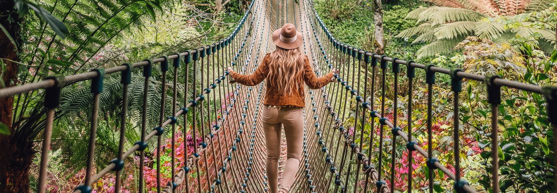 Young woman walking across a rope bridge surrounded by trees in Heligan, Cornwall