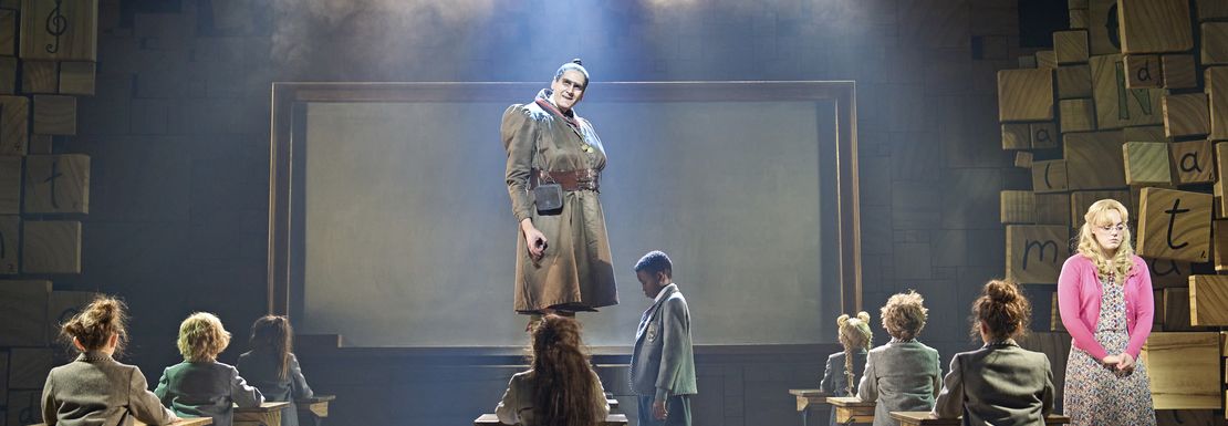 Miss Honey teaches her class as the children learn from her on stage