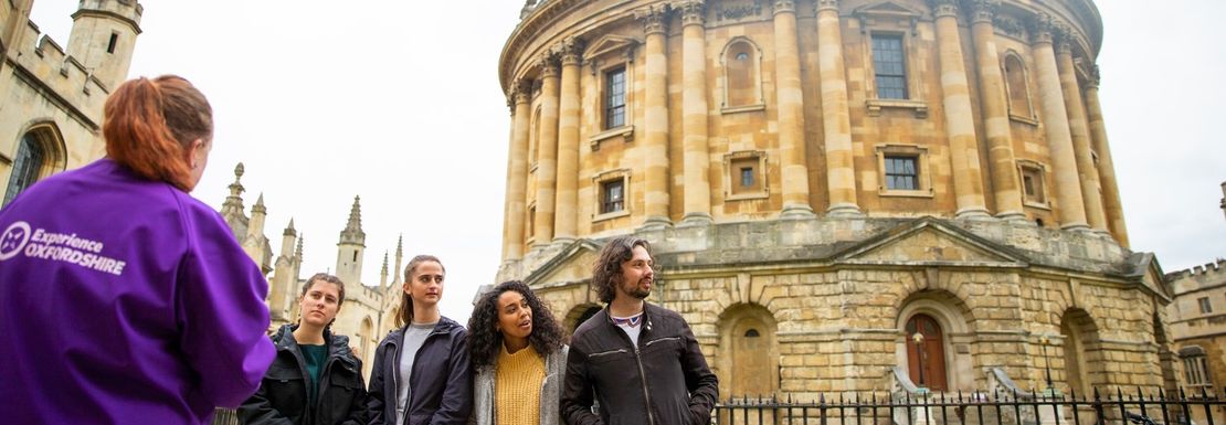 A tour guide leads a group on the Oxford walking tour and stops at an impressive building