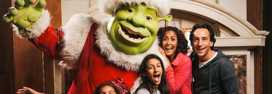 Shrek dressed in a Father Christmas outfit stands with a smiling and happy family