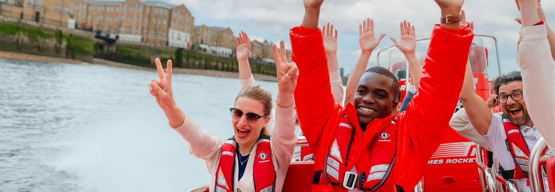 With hands in the air a groups speeds along on the river in London in a speedboat
