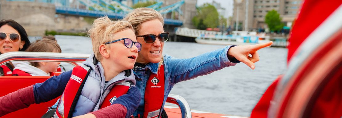 A mum and her son point whilst smiling on the Thames Rocket speedboat