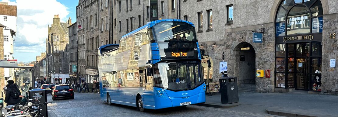 A blue double decker bus driving on a cobblestone street, adding charm to the picturesque scene.