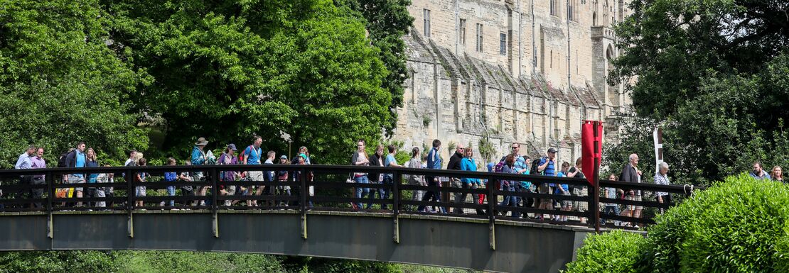 Visitors cross a bridge in front of Warwick Castle
