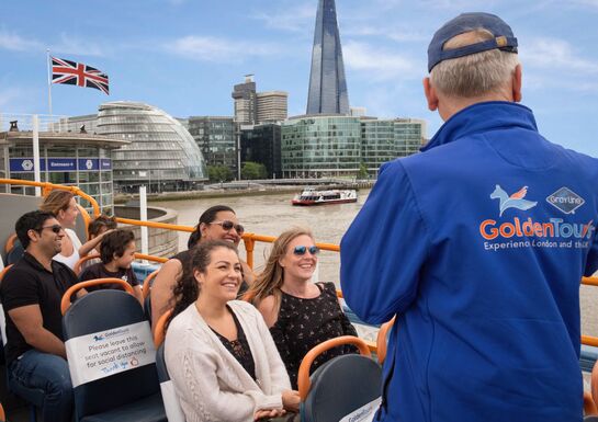 A tour guide engages in conversation with a group of people aboard the tour bus over the Thames River