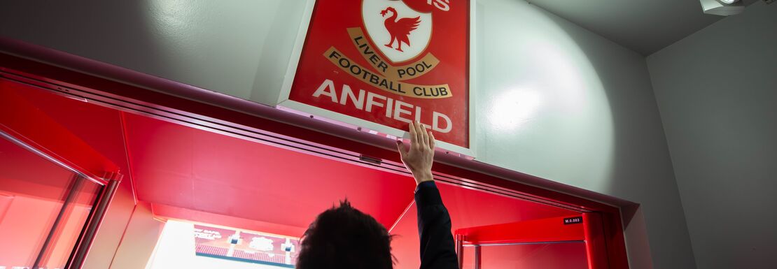 A Liverpool FC fan touching the 'This is Anfield' sign